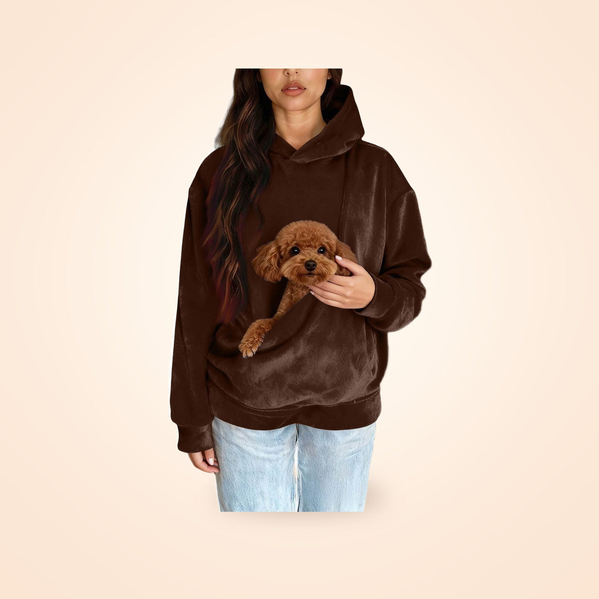 Person wearing a chocolate brown hooded sweatshirt with a toy poodle in the front pet pocket, on a warm cream background
