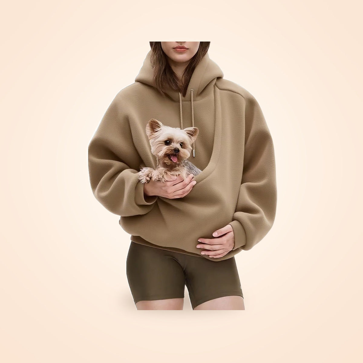 Person wearing a camel hooded pullover with a small terrier in the front pet pocket, on a warm cream background