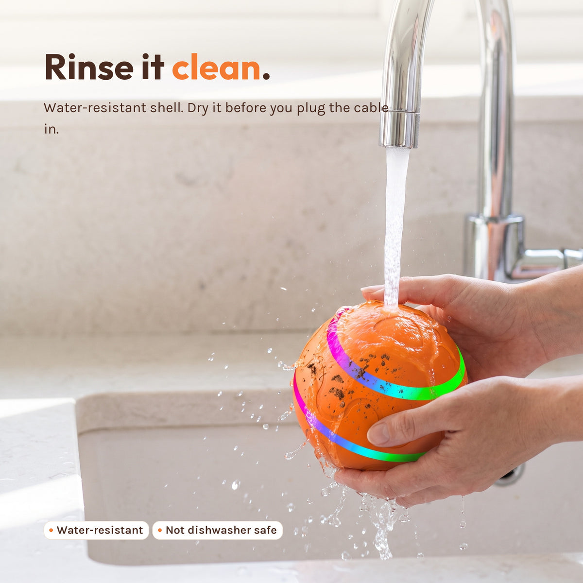 The ball being rinsed under a kitchen tap. Caption: rinse it clean. Water-resistant shell, dry it before you plug the cable in.